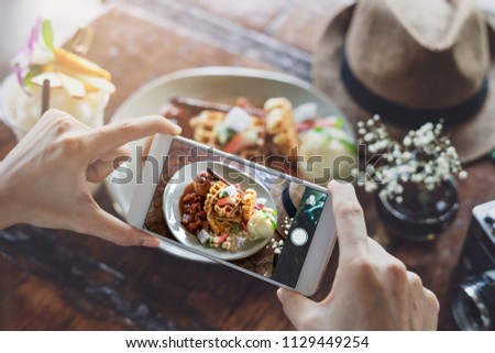 Young woman taking photo of food with smart phone in restaurant