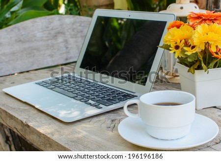 a cup of coffee and laptop on wood floor with flower