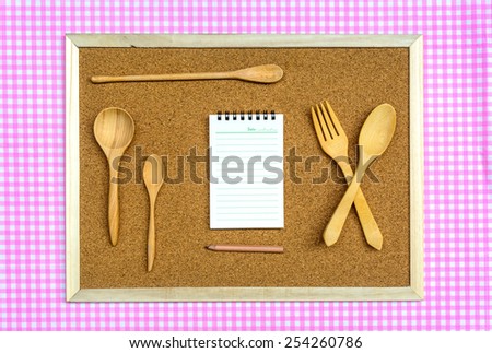 Wooden board with wooden spoon and notepad on tablecloth