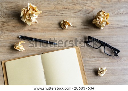 Crumpled paper balls with eye glasses and notebook on wood desk, creative writing concept
