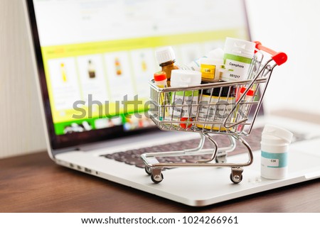 Mini shopping cart full of homeopathic remedies on laptop background. Homeopathy and internet online shopping concept.