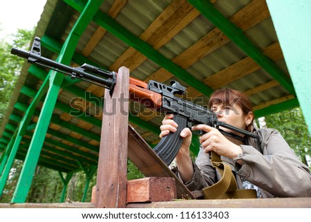 Young woman aiming at a target and shooting an automatic rifle for strikeball. Focus on the rifle.