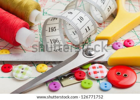 Sewing items: buttons, colorful fabrics, scissors, measuring tape, thimble, spools of thread on sewing pattern