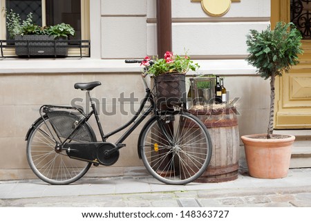 Old bicycle carrying flowers as decoration, wooden barrel with bottles of wine and tree in flower pot