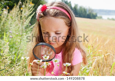 Little girl exploring the daisy flower through the magnifying glass outdoors