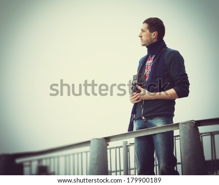retro stylized photo of young man photographer with vintage camera on a pier