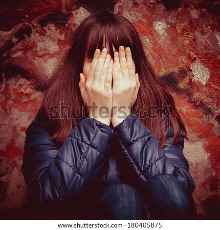 teenager girl with hands over eyes near dramatic red wall outdoors