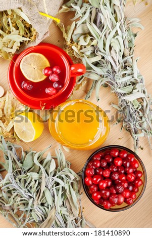 red cranberries, jar with honey, fruit tea cup, healing herbs and lemon on table, top view