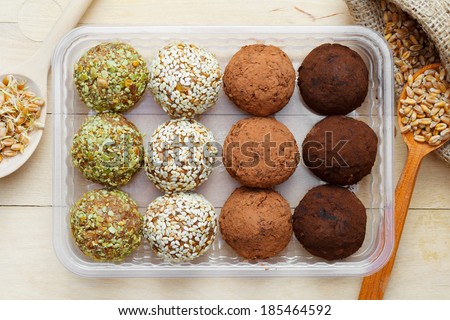 macrobiotic healthy food: balls from ground wheat sprouts with sesame, pumpkin seeds and chocolate sprinkles in plastic box; sprouted grains in wooden spoon on table, top view