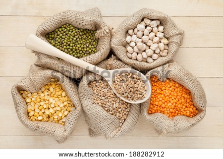 hessian bags with red lentils, peas, chick peas, wheat and green mung on wooden table