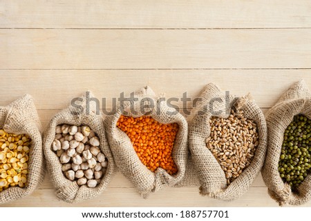 hessian bags with cereal grains: peas, chick peas, red lentils, wheat and green mung on wooden table