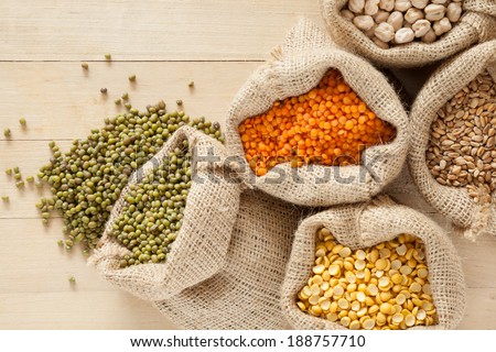 bags with cereal grains: red lentils, peas, chick peas, wheat and green mung on wooden table