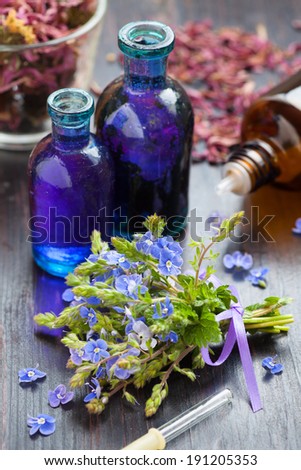 glass bottle of essential oil and blue healing flowers on wooden table