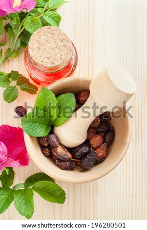 essential oil in glass bottle, dried rose-hip berries in wooden mortar and rose hip flowers on table, top view