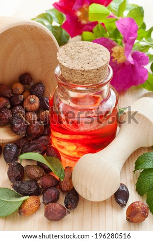 essential oil in glass bottle, dried rose-hip berries and rose hip flowers on table