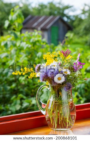 bouquet of summer flowers and healing herbs in jug on windowsill