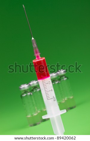 syringe with red  content and medical ampules on green background
