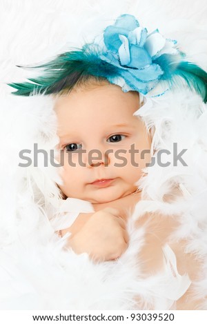 beautiful adorable baby with fashion flower in her hair, lying in fluffy feathers