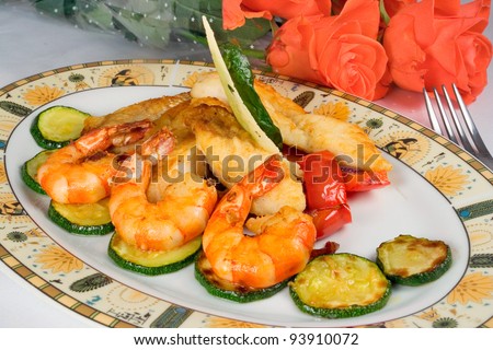 tasty dish: fried fish fillets, shrimp, zucchini on plate, bouquet of roses lying beside