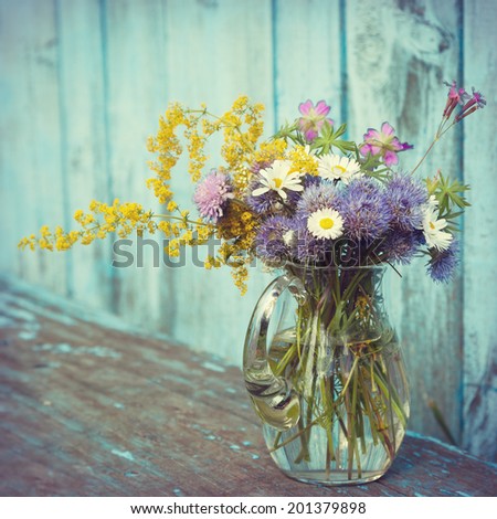 bouquet of garden flowers and healing herbs in glass jug on old wooden bench