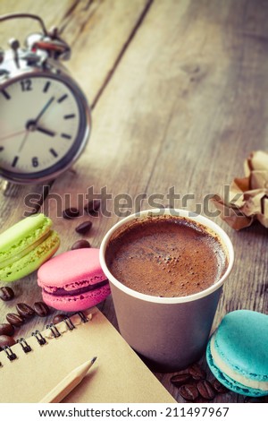macaroons, espresso coffee cup, sketch book and alarm clock on wooden rustic table, vintage stylized photo