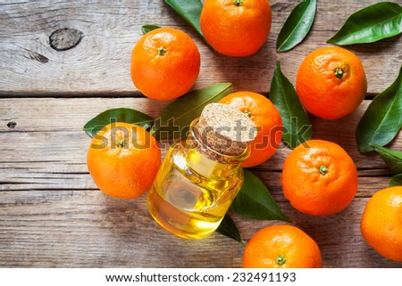Ripe tangerines with leaves and bottle of essential citrus oil on a wooden table.