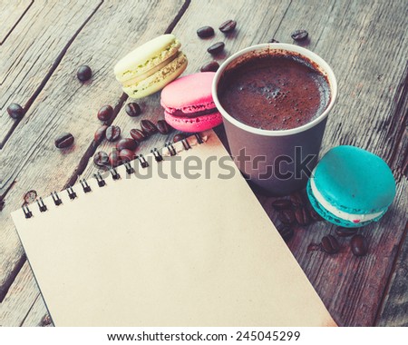 Macaroons cookies, espresso coffee cup and sketch book on wooden rustic table, vintage stylized photo