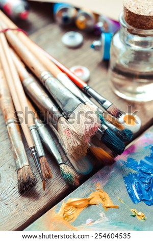 Vintage stylized photo of paintbrushes closeup, artist palette and multicolor paint tubes.