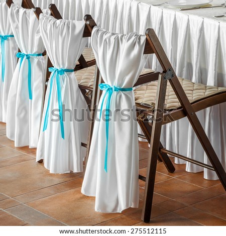 Row of wedding chairs, decorated with white fabric and blue ribbons.