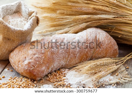 Fresh bread, sack of flour and wheat ears on wooden table.