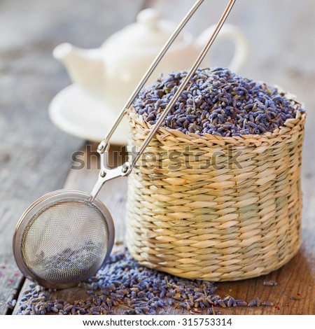 Lavender herbal tea in basket, tea infuser and teapot on background. Selective focus.