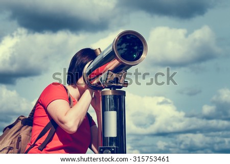 Young woman looking through tourist telescope, exploring landscape.