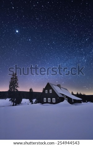 Alone and abandoned cottage house in the snowy nature in the night under the sky full of stars.