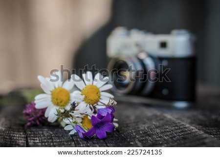 On wooden boards are wildflowers near the old camera
