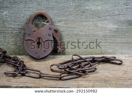 The old rusty padlock with keys lying on textured wooden boards. Around him wrapped rusty metal chain.