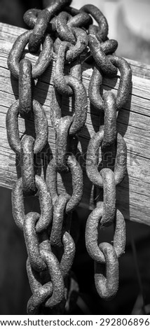 Old rusty metal chain with large links, hanging on a wooden board.