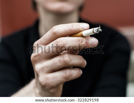 Woman in a very bad mood, holding in his hand, holding a smoldering between his fingers (fuming) cigarette. Cigarette close-up.