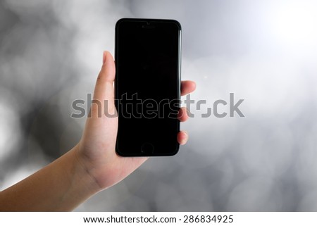 woman hand holding smart phone on blurred bokeh nature background in black white tone with path