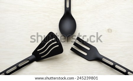 Pieces of black kitchen utensil set that looks like fork and spoon for pots and pans with non-stick coating on wooden table surface with some room for text.