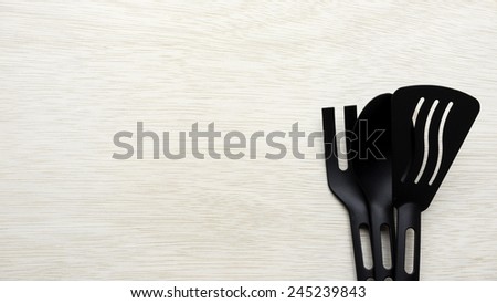 Pieces of black kitchen utensil set that looks like fork and spoon for pots and pans with non-stick coating on wooden table surface with some room for text.