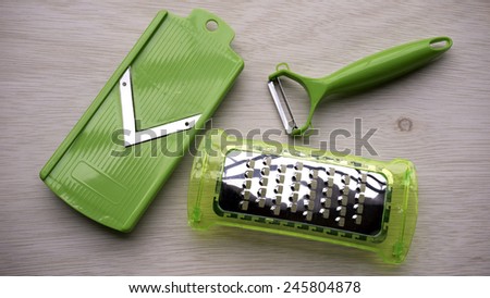 Pieces and set of stainless steel green color precision modern cutting food slicer or dicer for fruit, cheese, sausage and vegetables on wooden table surface with some room for text.