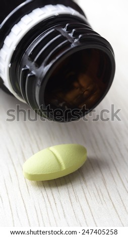 Yellow pills on wooden surface. Pills spilling from container. Copy space. Slightly defocused and closeup shot.