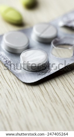 White pills strip and yellow pills on wooden table. Copy space. Slightly defocused and closeup shot.