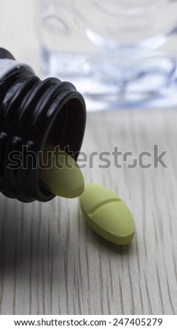 White and yellow pills white mineral bottle on table. Pills spilling from container. Copy space. Slightly defocused and closeup shot.