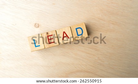 Block of alphabet letters forming the word LEAD on wooden surface. Concept of common marketing business terms. Slightly defocused and close-up shot. Copy space.