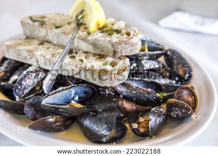 Plate of steamed mussels in sauce with bread, cheese and lemon