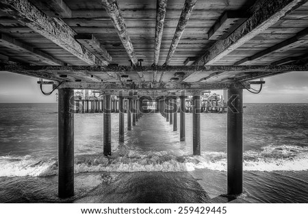 The underside of a pier with rest area on the end of it, black and white