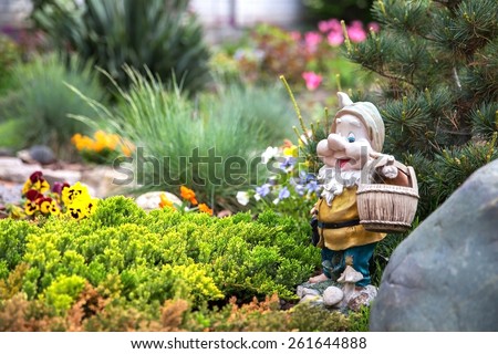 Funny garden gnome standing among nice flowers