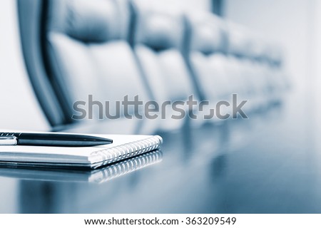 Notepad for agenda kept on table in empty corporate conference room before business meeting in blue tone