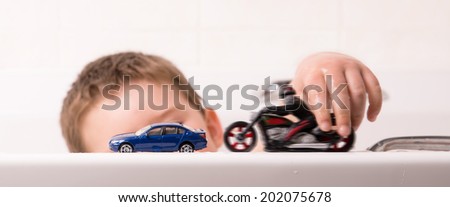 Child playing in bath with car and bike toys